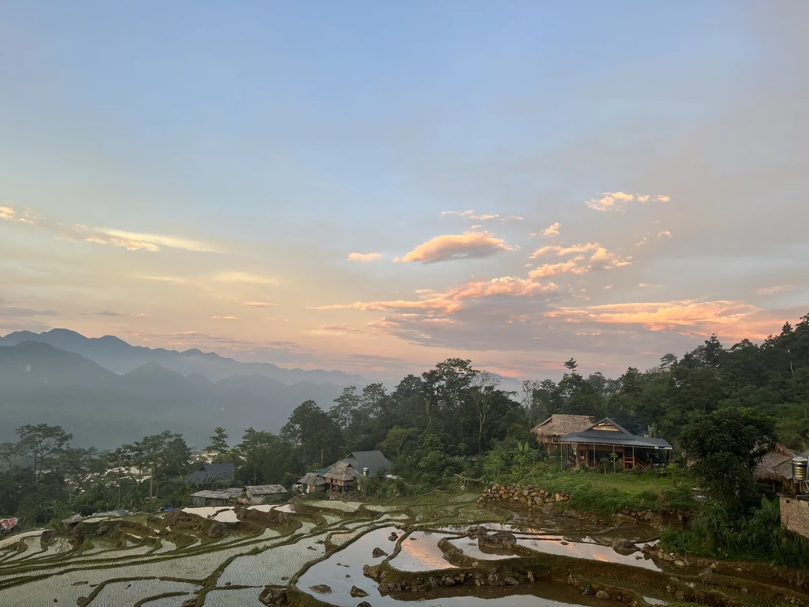 Sunset colors the sky over water-filled rice terraces and mountain ridges in Pu Luong.