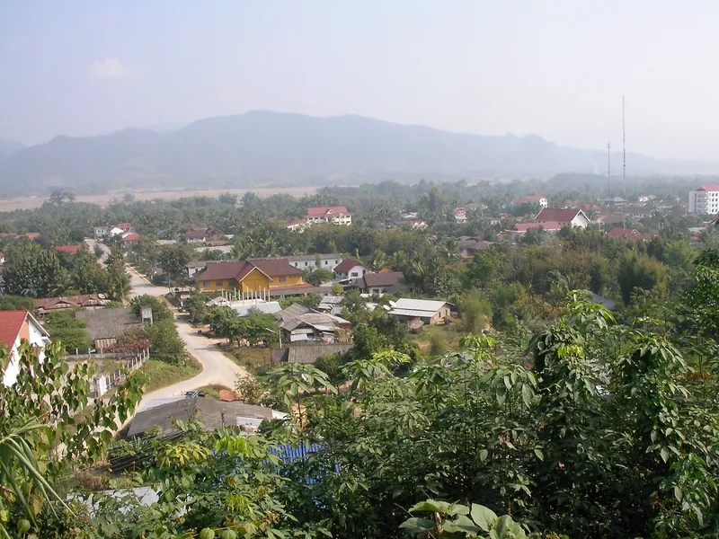 Elevated view over Luang Namtha town's rooftops and green trees with mountains in the hazy background.