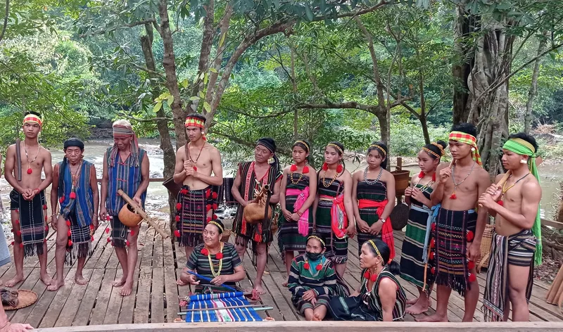 A group of Bunong people in traditional ceremonial clothing gathers on a wooden platform in Mondulkiri, Cambodia.