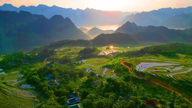 Sunrise light spreads across water-filled rice terraces and forested hills in Pu Luong valley.