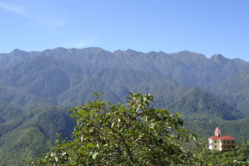 A red-roofed building sits below the rugged Hoang Lien mountain range near Sapa.