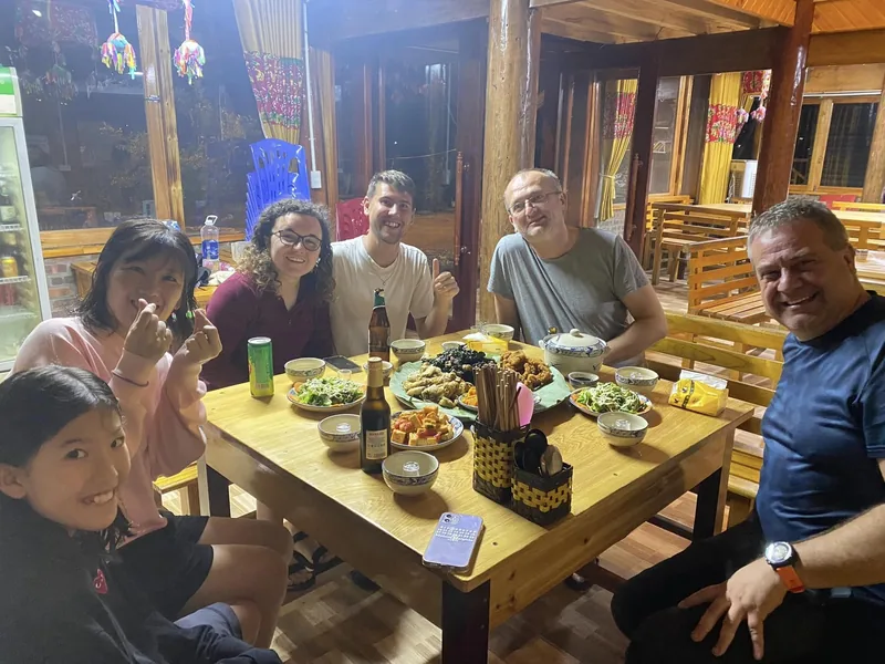 Travelers gather around a wooden table sharing a home-cooked meal at a stilt house restaurant near Fansipan, Lao Cai.